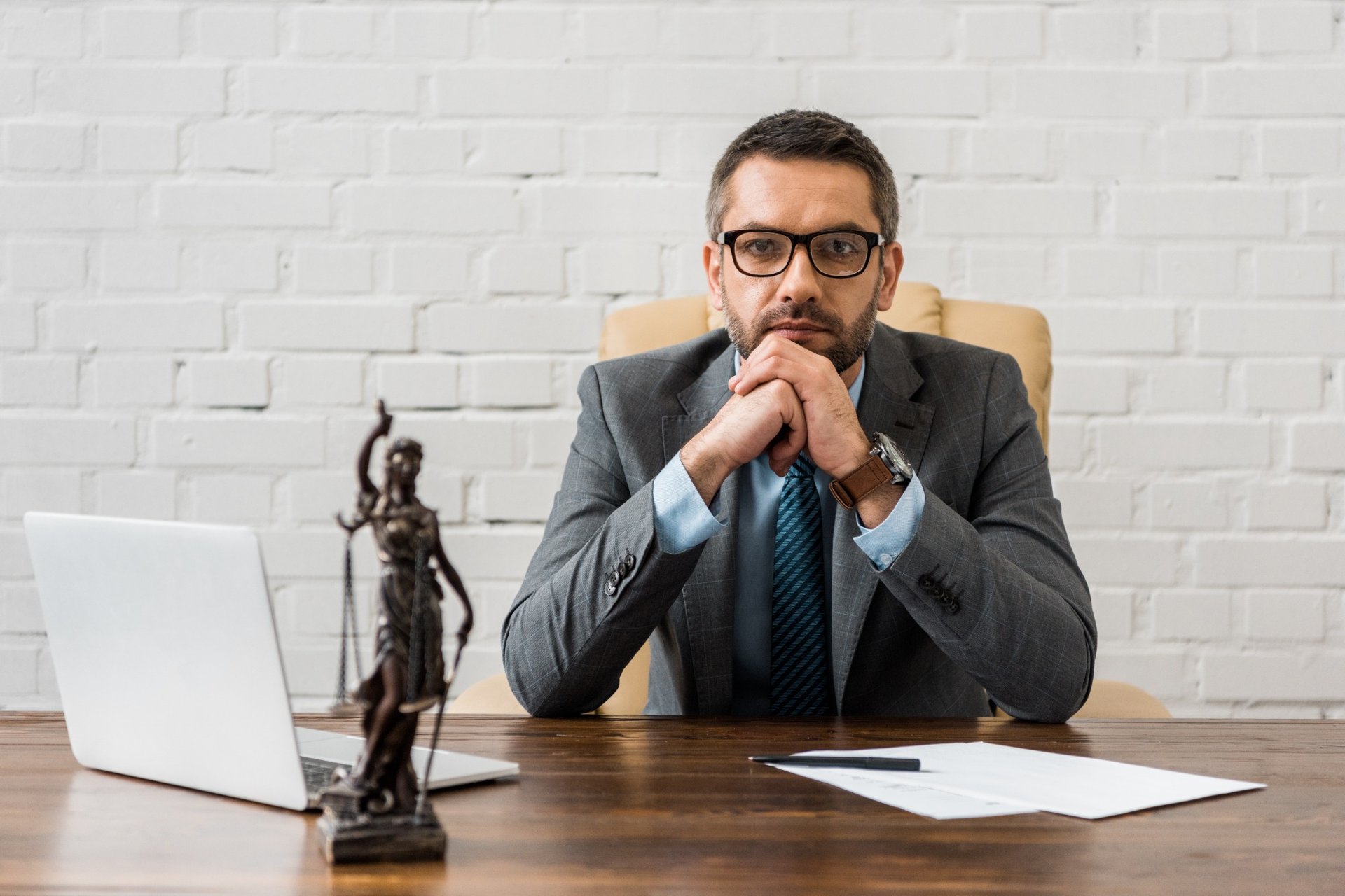 Confident male lawyer in suit sitting at desk with justice statue