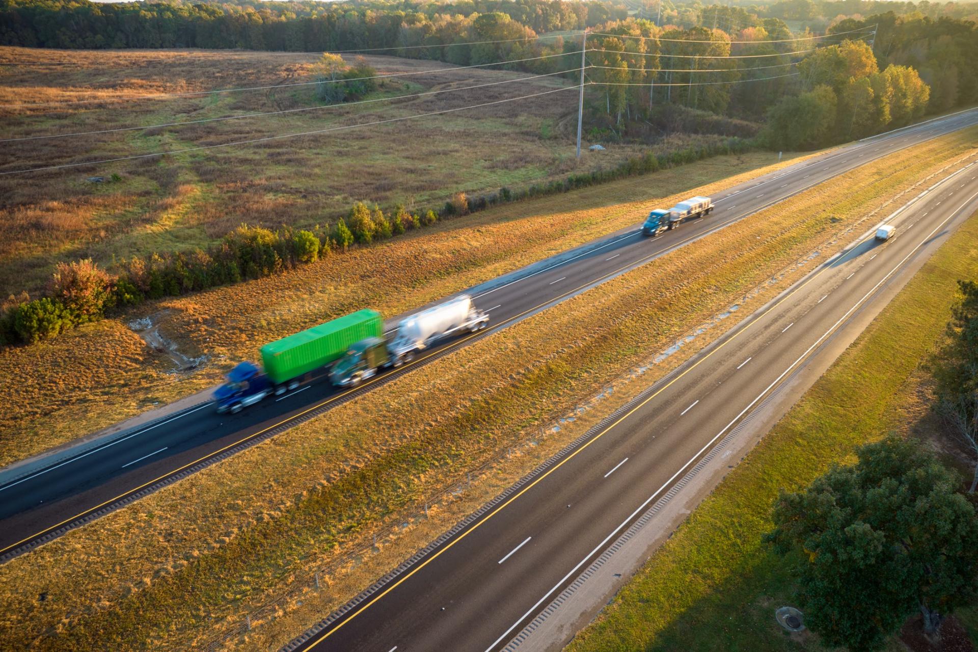Aerial view of multiple semi-trucks and cars traveling along a wide American highway during golden hour