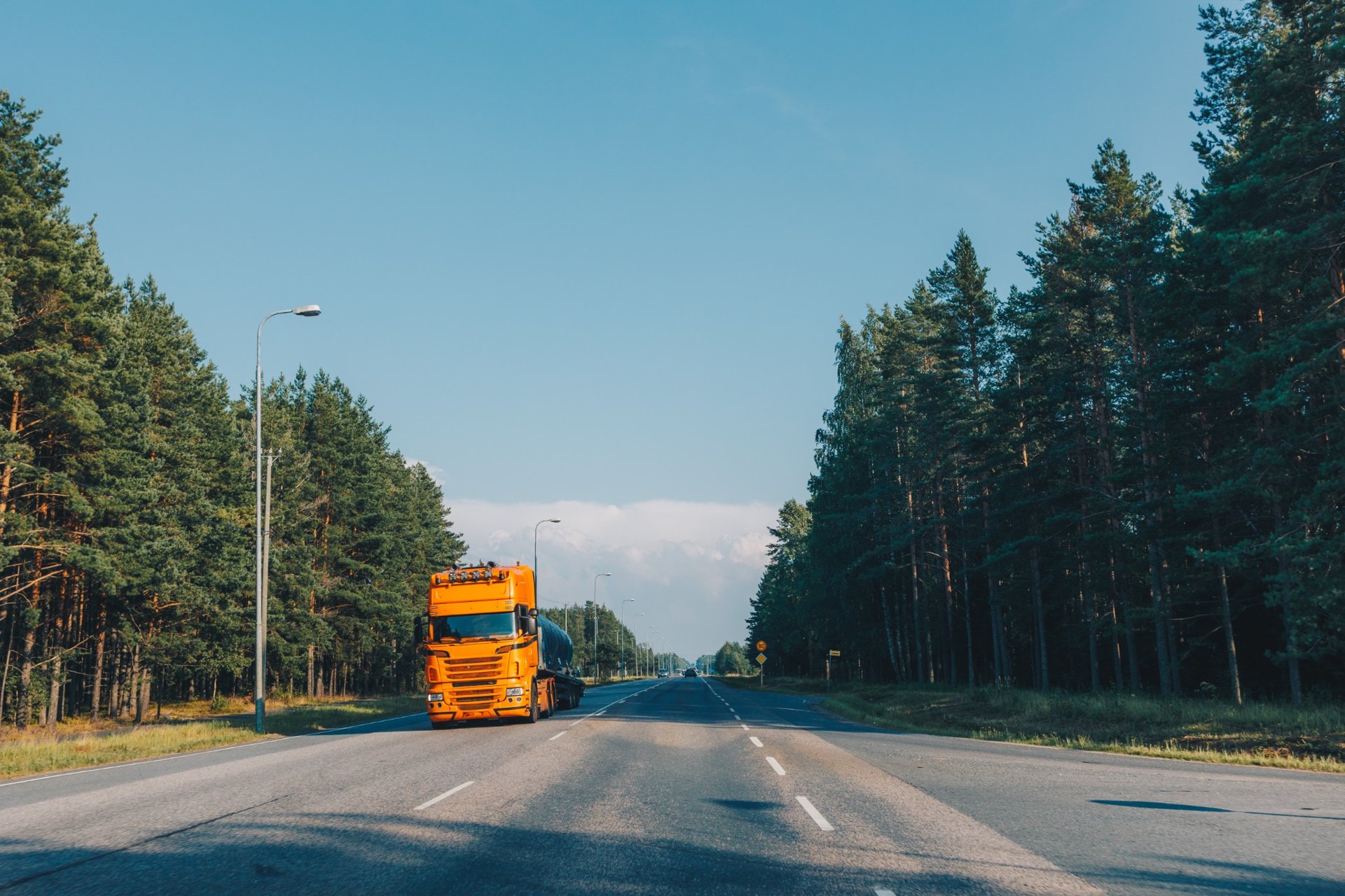 Bright orange fuel tanker truck driving on a forest highway