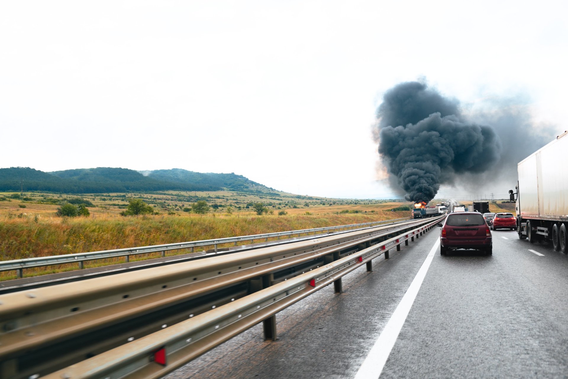 Dark smoke and flames rising from a vehicle fire on a busy highway, causing traffic congestion