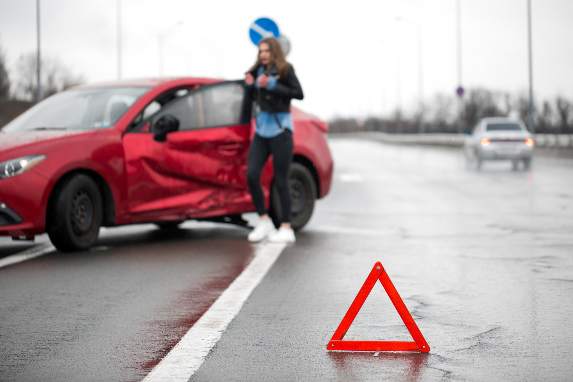 Driver sitting at roadside after traffic accident. Focus is on the red triangle sign.