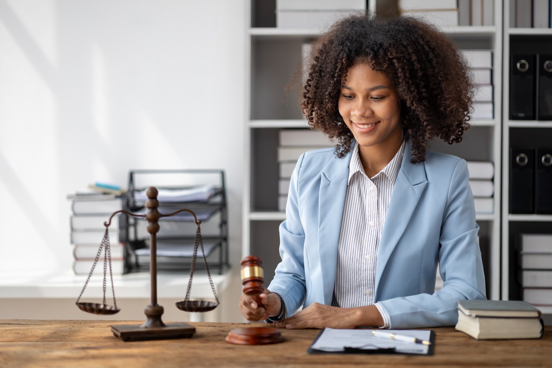 Female lawyer with gavel and justice scales, smiling while seated at her office desk