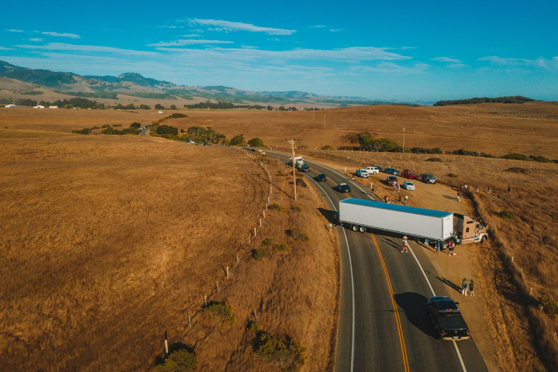 Semi-truck blocking a rural highway curve as people and cars gather around the accident site