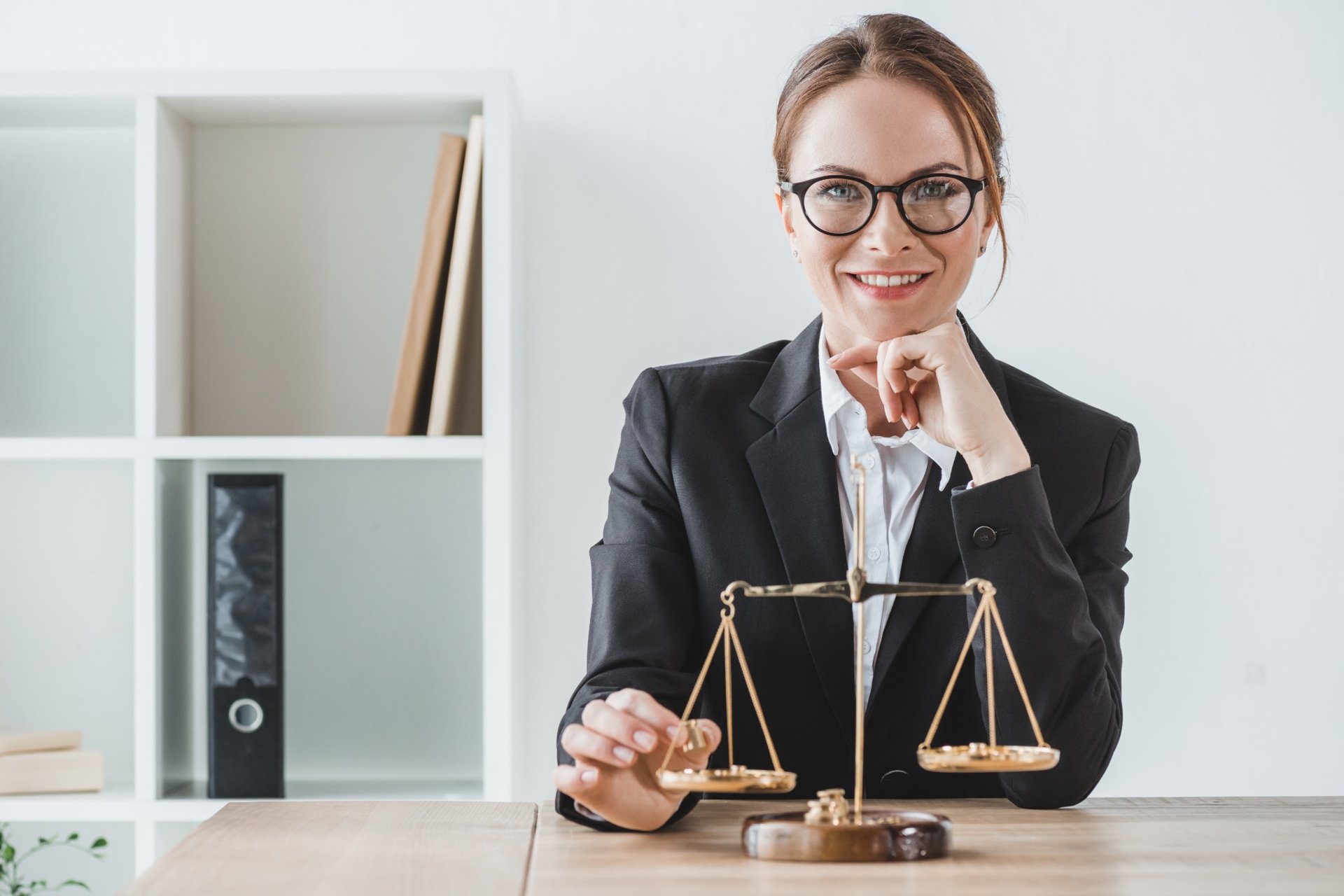 Smiling lawyer in glasses sitting at desk with justice scales in front of her