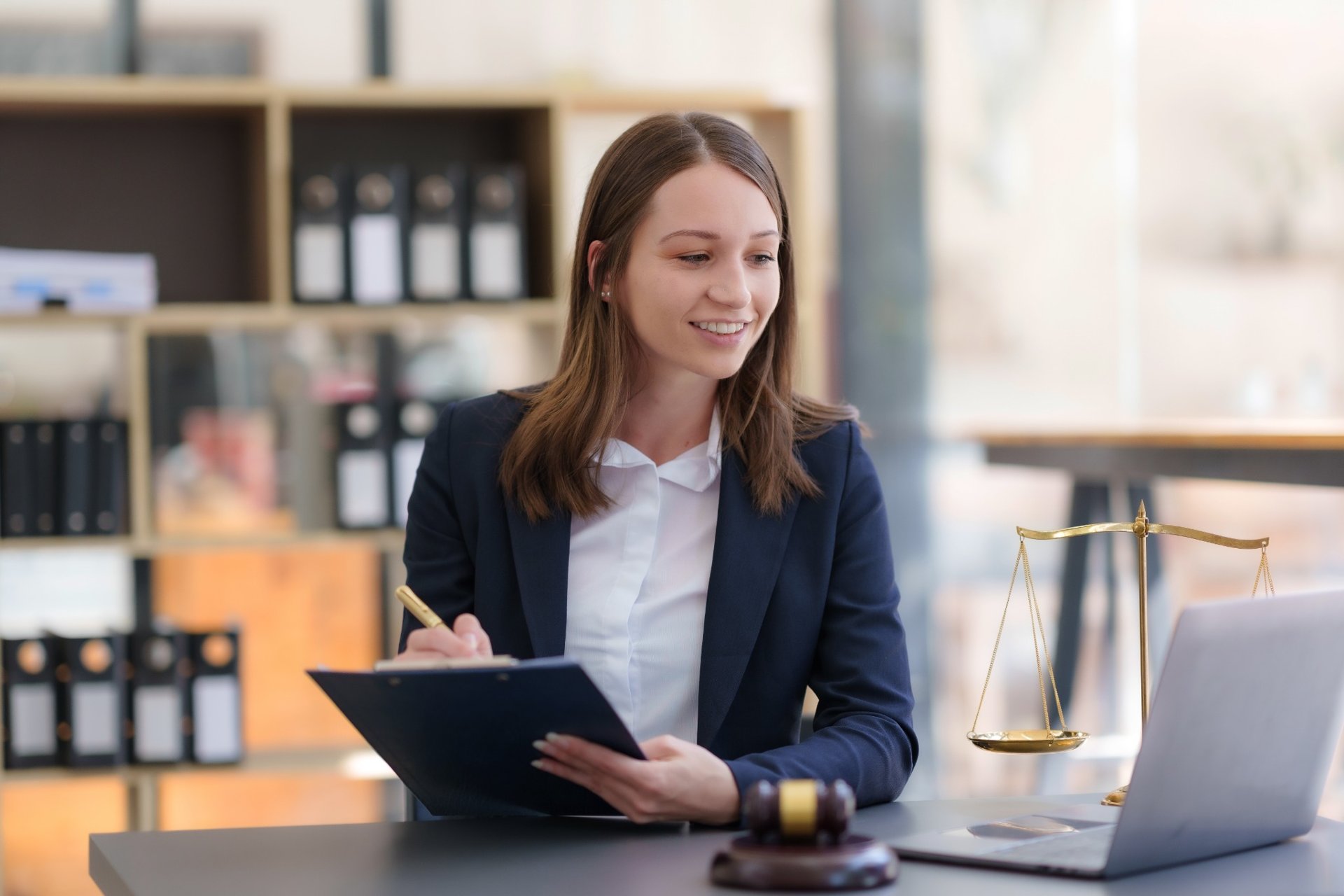 Young female lawyer smiling while taking notes during an online meeting in a modern office