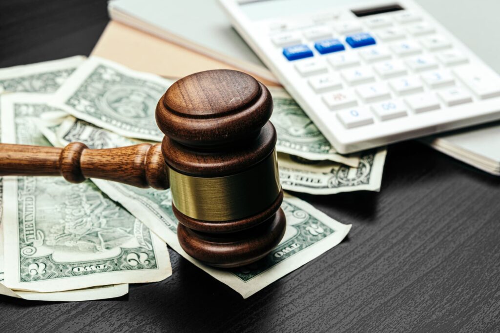 Wooden judge gavel on dollar bills beside calculator symbolizing legal fees and financial judgment